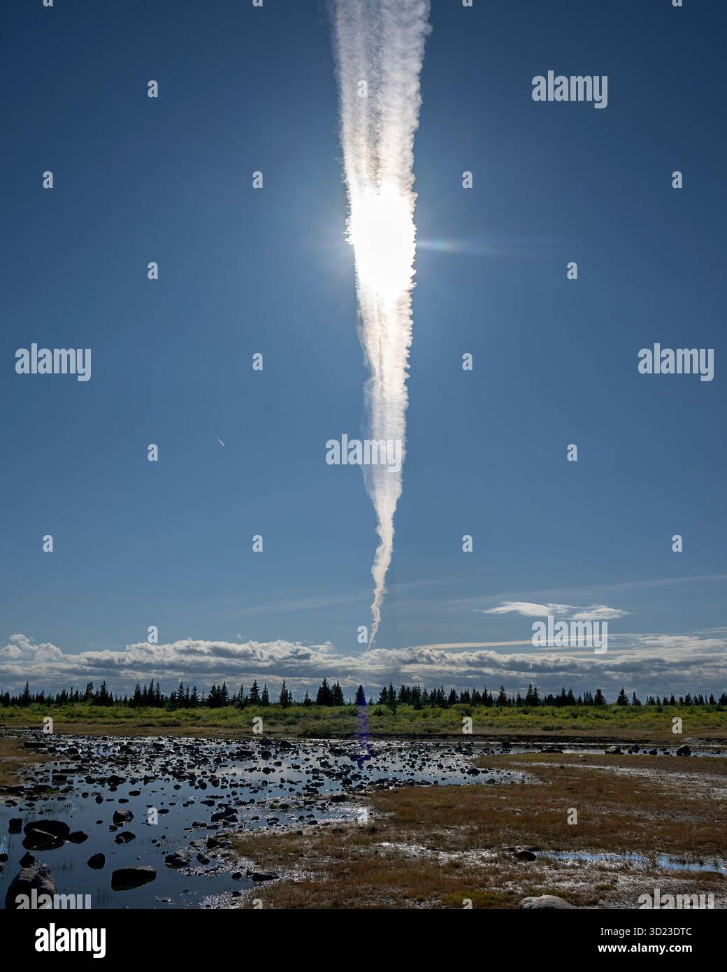 Vertikaler Kondensstreifen gegen blauen Himmel über einer felsigen Landschaft mit kleinen Teichen und weit entfernten Bäumen. Hudson Bay, Churchill, Manitoba, Kanada Stockfoto