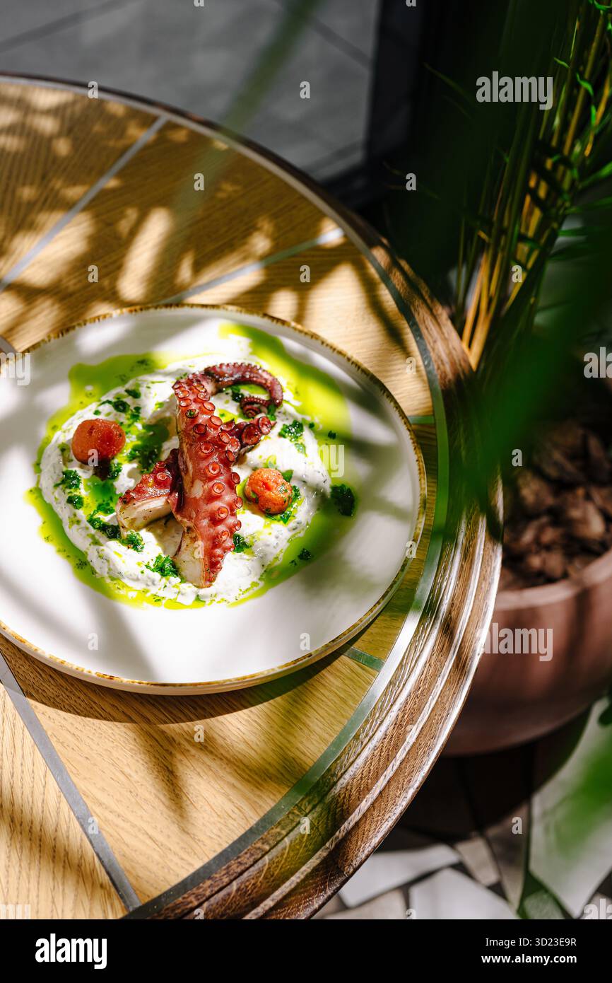Köstliches Oktopusgericht mit lebendiger grüner Sauce auf einem Holztisch Stockfoto