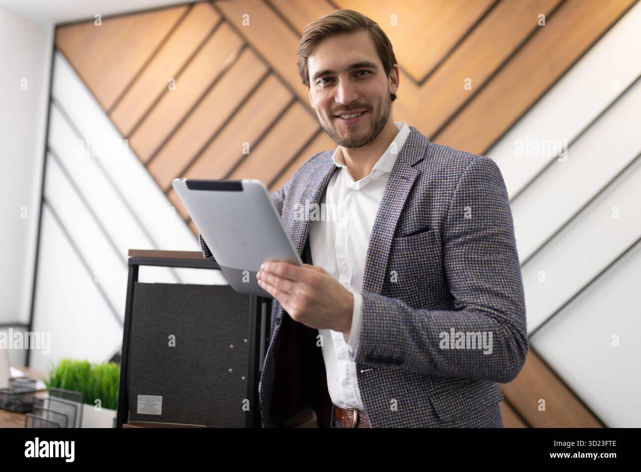 Junger männlicher Geschäftsmann mit einem Tablet in der Hand auf dem Hintergrund des Büros Stockfoto