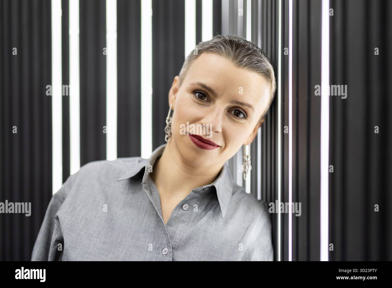 Porträt einer stilvollen kurzhaarigen Frau in einem grauen Hemd vor einer schwarzen Wand mit Hintergrundbeleuchtung Stockfoto