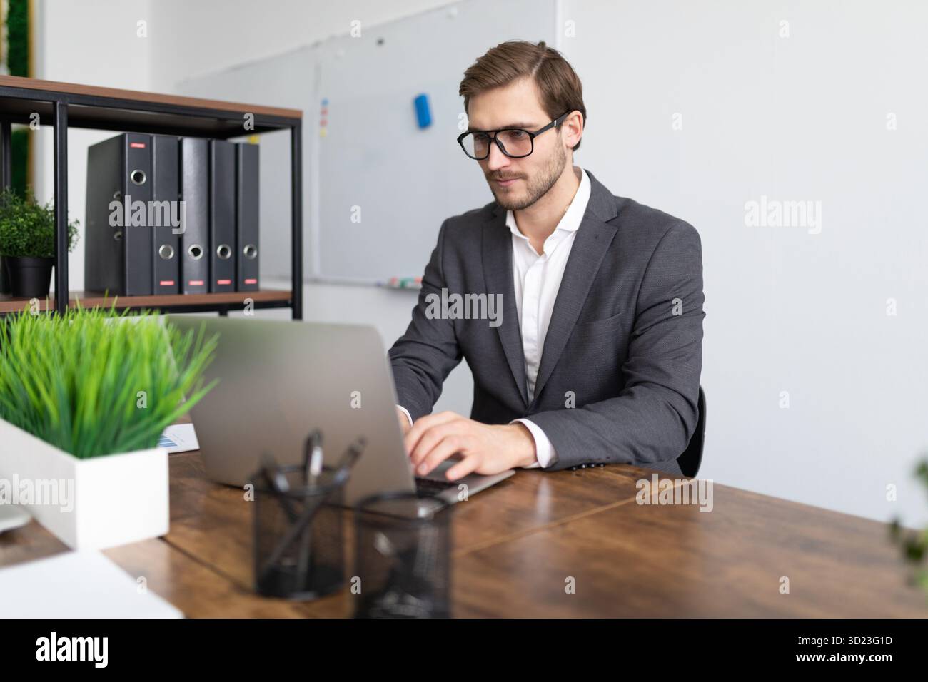 Geschäftsmann an einem Laptop im Büro in einem formellen Anzug mit Brille Stockfoto