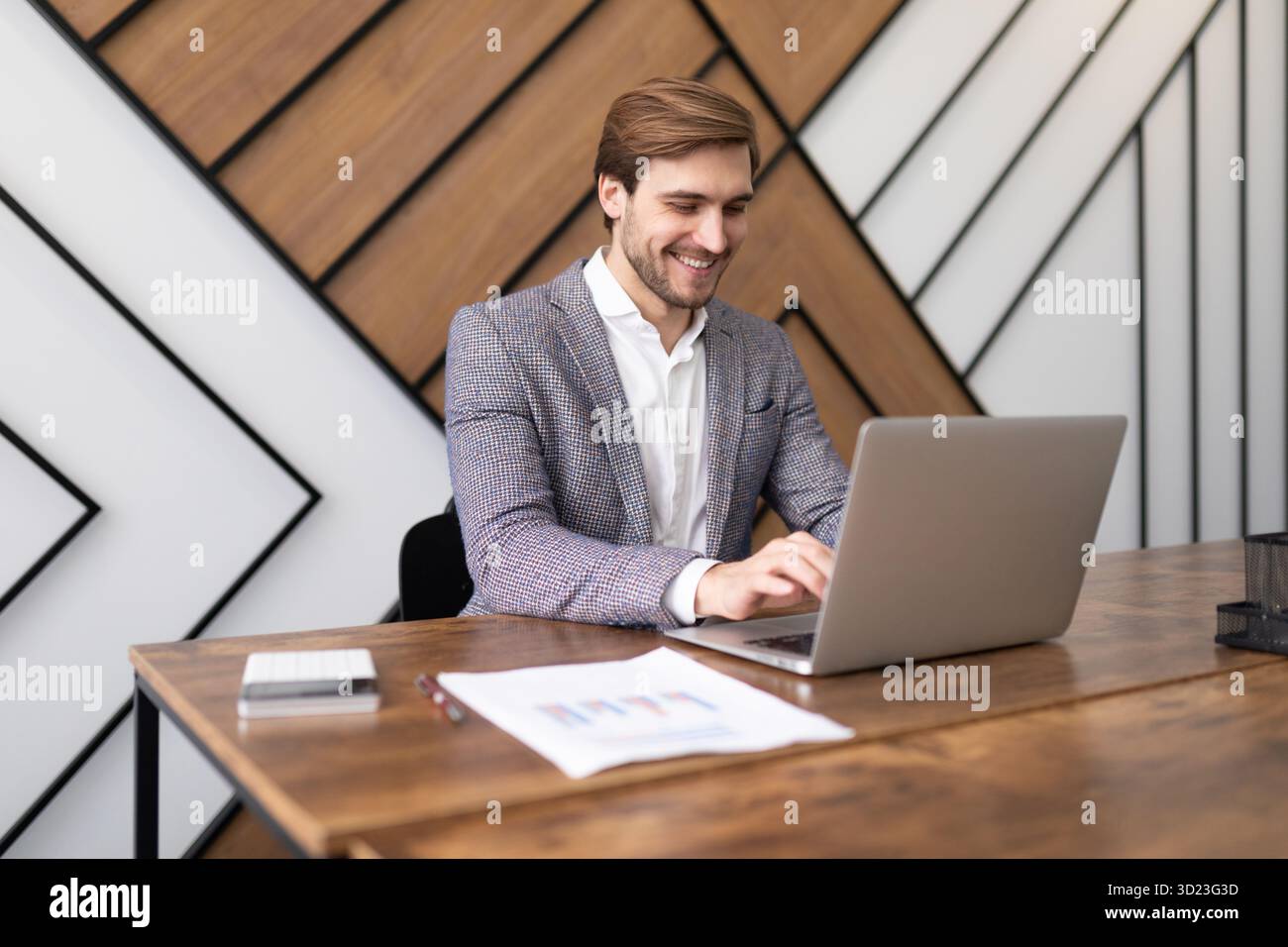 Ziemlich erfolgreicher Geschäftsmann, der im Büro an einem Laptop arbeitet Stockfoto