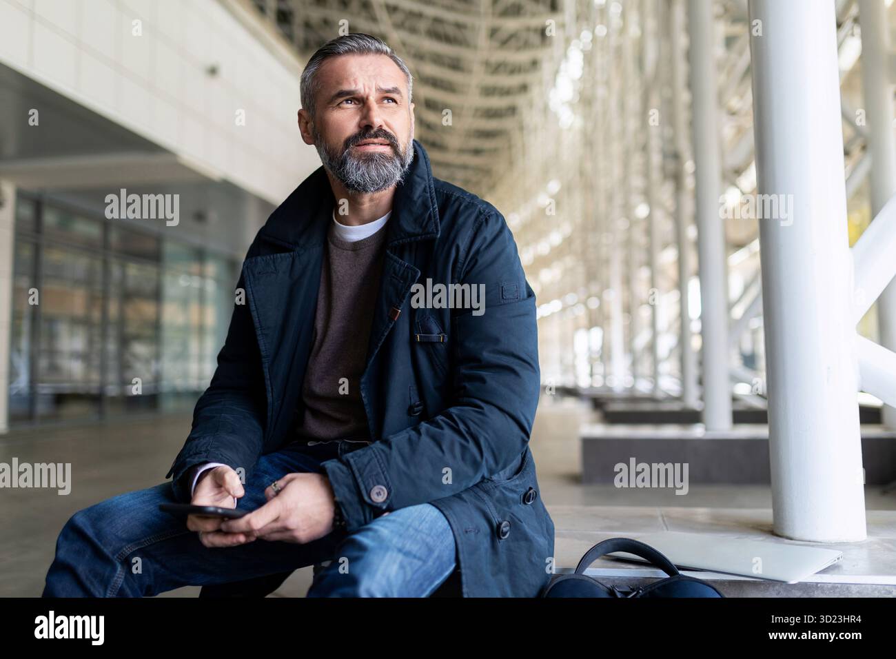 Erwachsener bärtiger Geschäftsmann, der auf das Einsteigen in ein Flugzeug im Flughafengebäude wartet Stockfoto