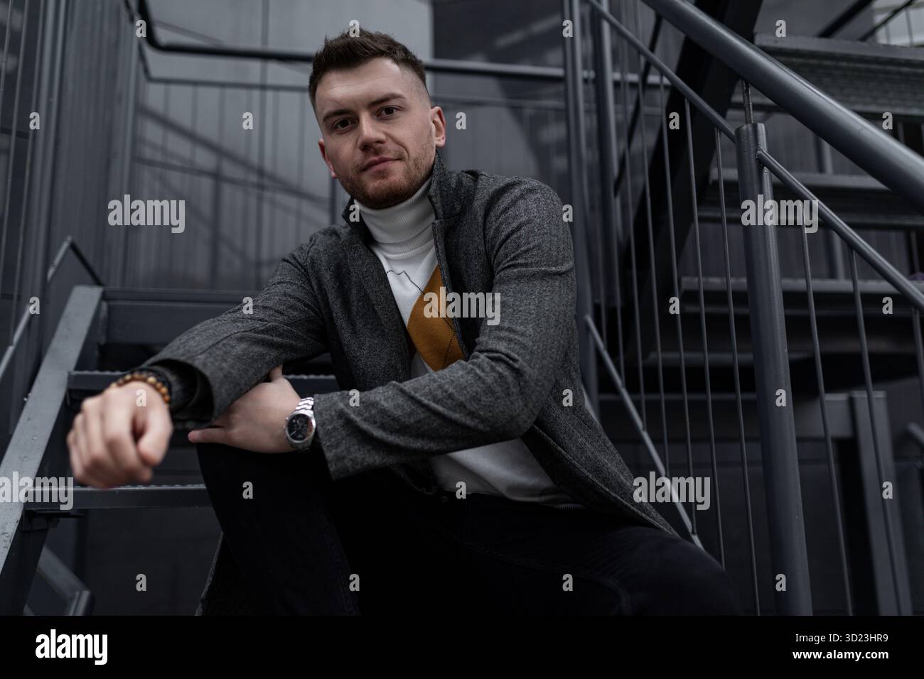 Stilvoller, eleganter junger Mann aus dem kaukasus, der draußen auf schwarzen Stufen sitzt Stockfoto