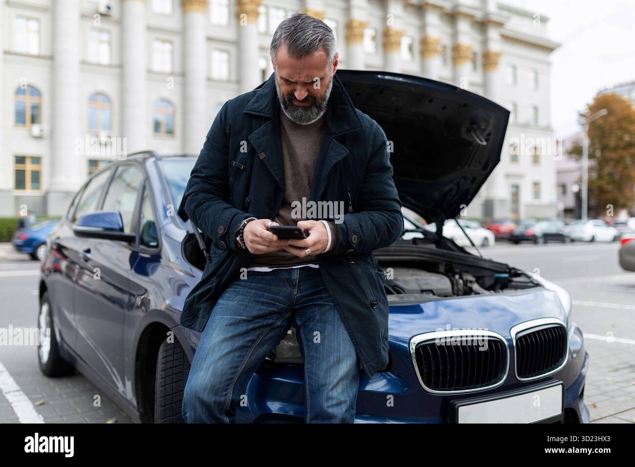 Ein Erwachsener ruft den technischen Support für eine Autoreparatur neben einem kaputten Auto mit offener Motorhaube an Stockfoto