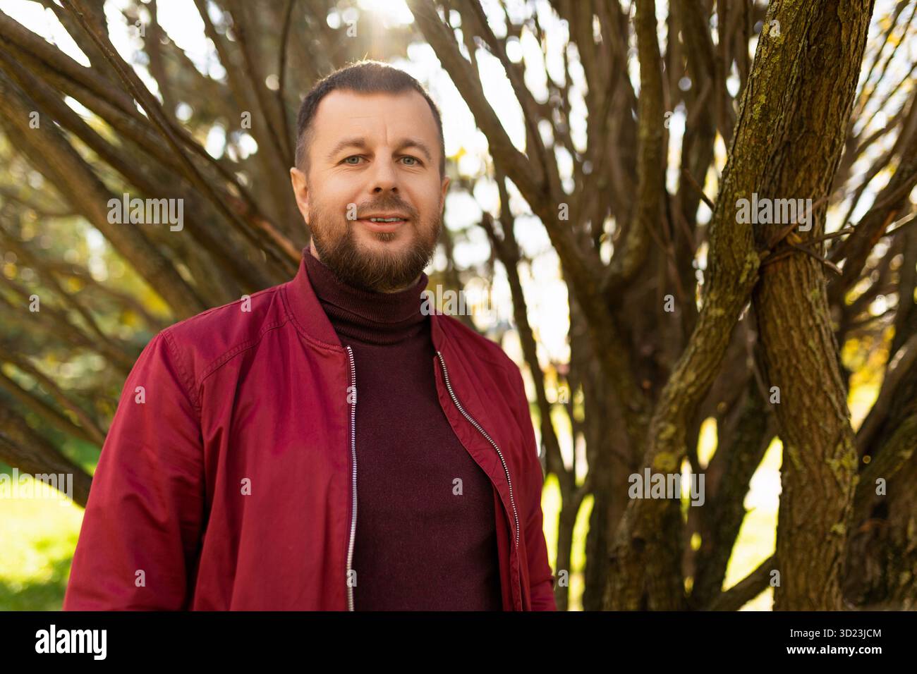 Lächelnder junger Mann mit Bart in roter Jacke im Herbstpark Stockfoto