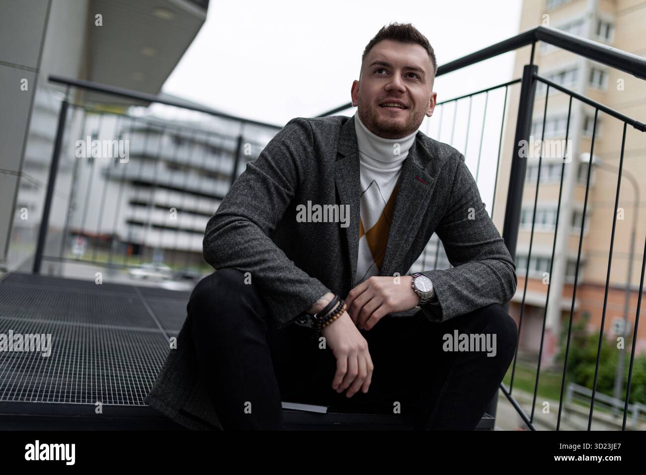 Stilvoller eleganter kaukasischer Mann, der auf Stufen sitzt und lächelnd in die Kamera blickt Stockfoto