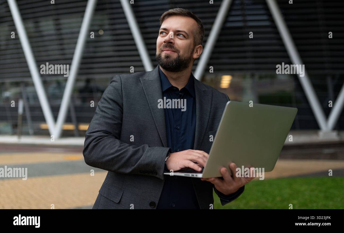 Erwachsener Geschäftsmann mit Laptop auf dem Hintergrund eines Bürogebäudes, betriebswirtschaftliches Beratungskonzept Stockfoto