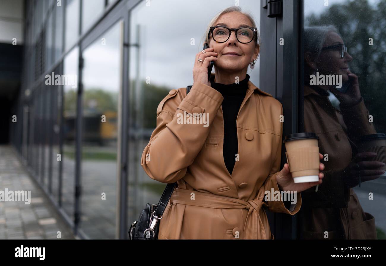 Eine ältere Geschäftsfrau geht zur Arbeit und spricht mit einem Mobiltelefon, eine Führungskraft im Geschäftskonzept Stockfoto