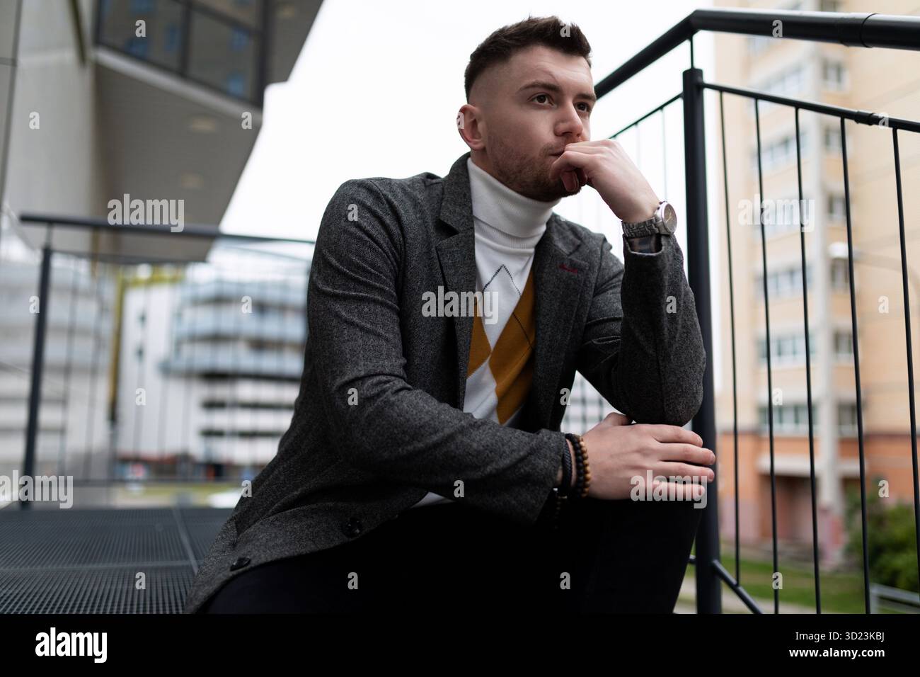 Porträt eines nachdenklichen jungen Mannes, der auf der Treppe neben seinem eigenen Gebäude sitzt Stockfoto