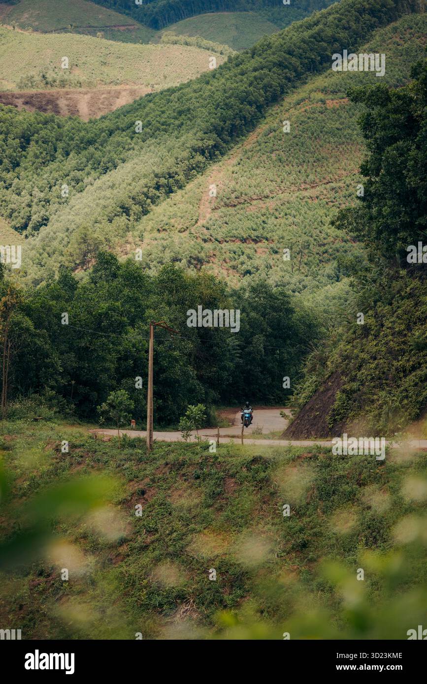 Ein einsamer Radfahrer fährt auf einem gewundenen Pfad durch üppige, grüne Hügel und dichte Wälder. Son Dong District, Bac Giang, Vietnam Stockfoto