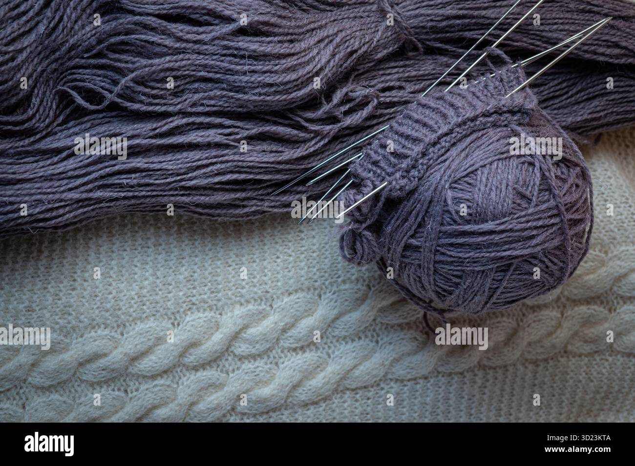 Ein Ball aus purpurroter Wolle und Stricknadeln auf weißem Hintergrund. Stockfoto