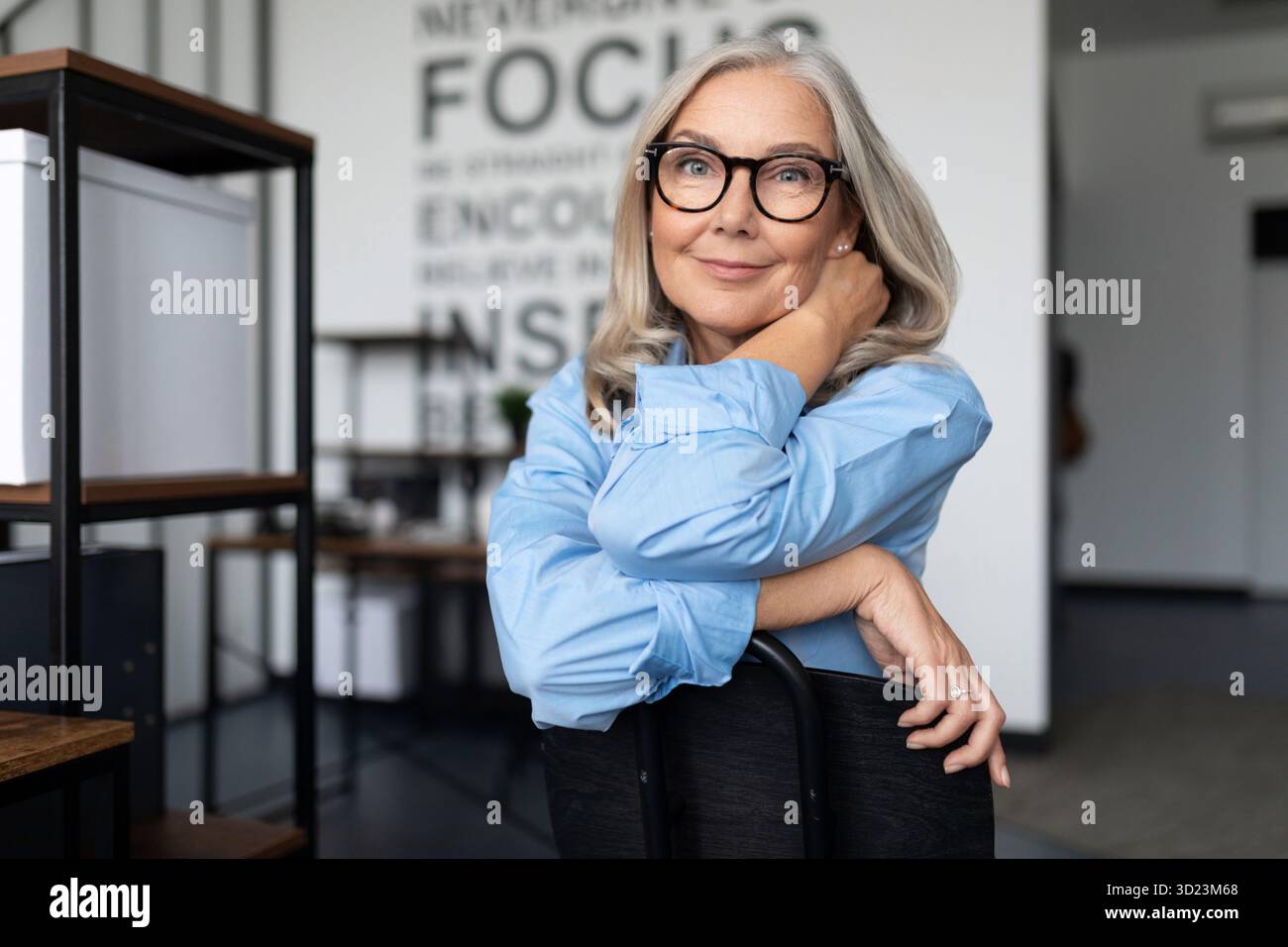 Nahporträt einer starken Anführerin, 50 Jahre alt, die auf einem Stuhl vor dem Hintergrund eines modernen Büros sitzt. Business In Stockfoto