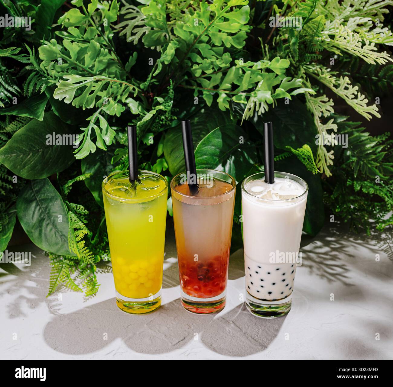 Farbenfrohe Getränke werden an einem warmen Nachmittag vor einer üppigen grünen Kulisse präsentiert Stockfoto
