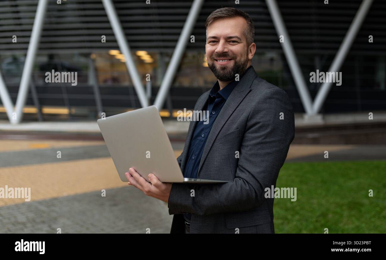 Männlicher Geschäftsanalyst mit einem Laptop auf dem Hintergrund eines Bürogebäudes Stockfoto