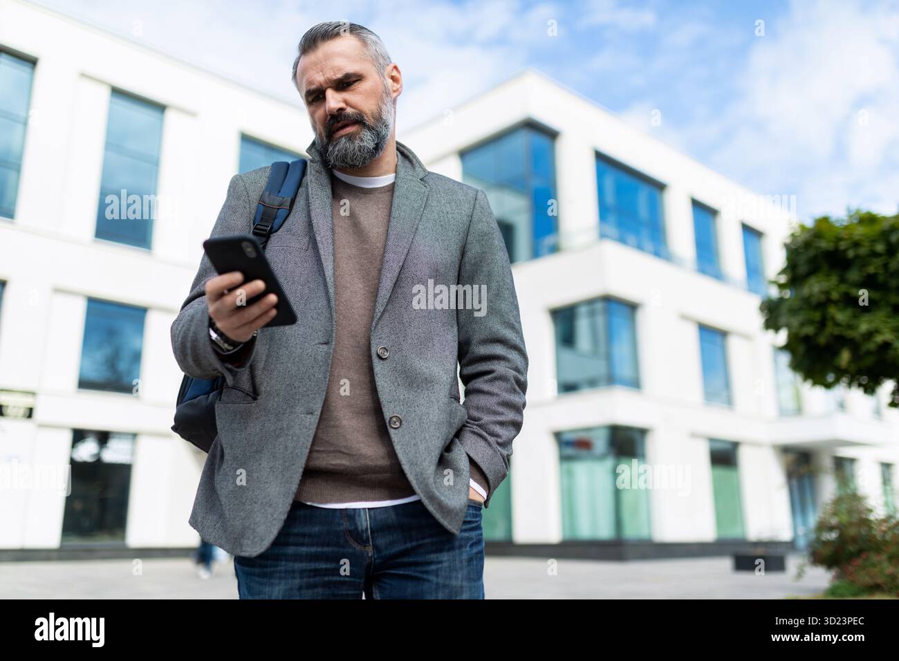 Erwachsener männlicher Software-Ingenieur verlässt das Büro und schaut sich das Handy an Stockfoto
