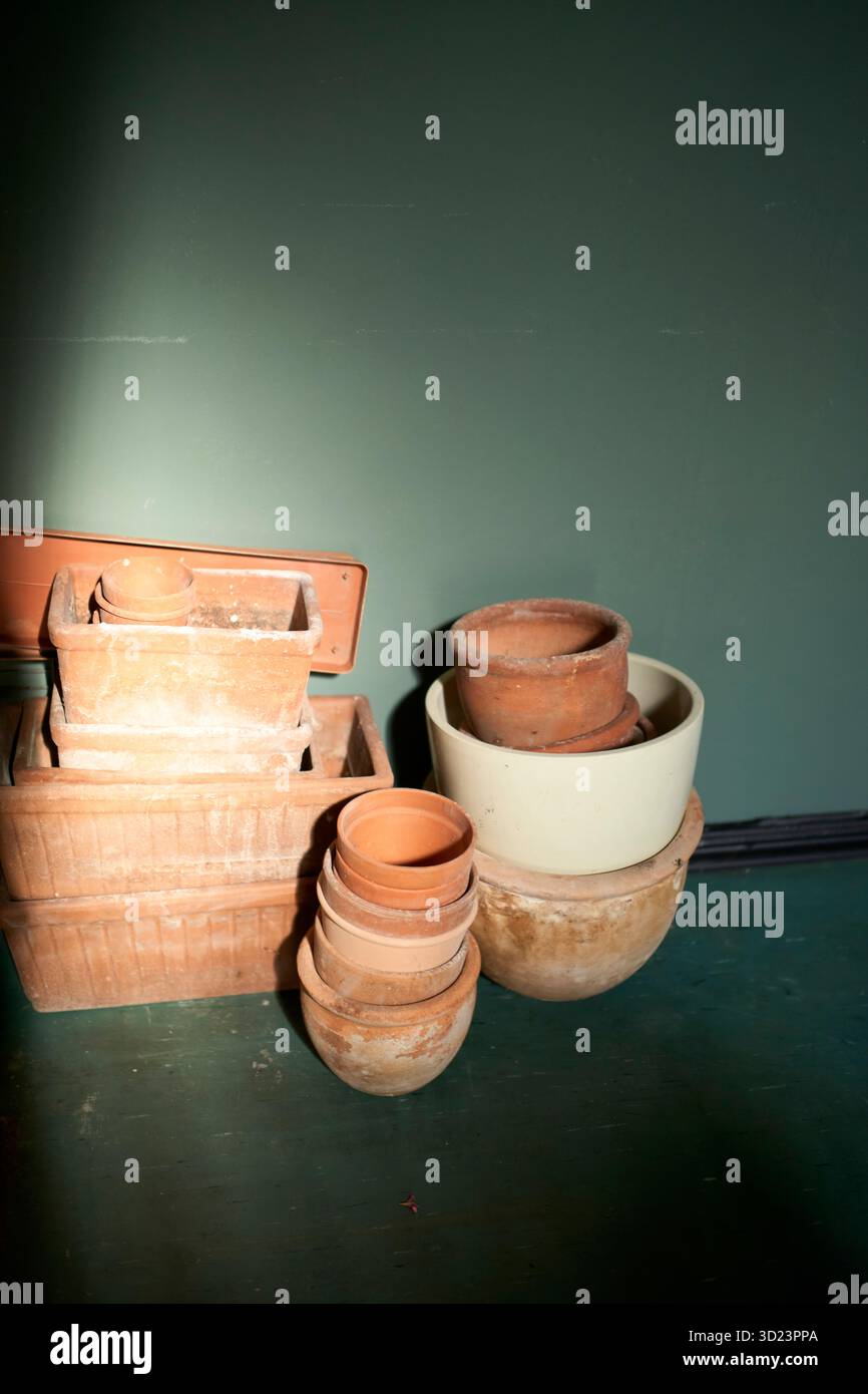Gestapelte Terrakotta-Töpfe und -Schüsseln auf grünem Boden vor einer dunklen Wand. Stockfoto