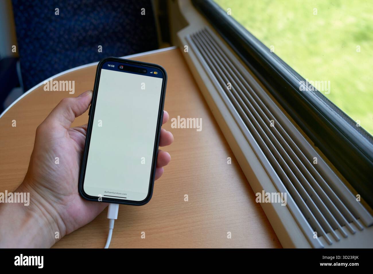 Hand hält ein Smartphone mit leerem Bildschirm in einem Zug an einem Fenster mit grüner Landschaft draußen. Salzkammergut, Salzdomäne, Dachsteingebirge, Österreich Stockfoto