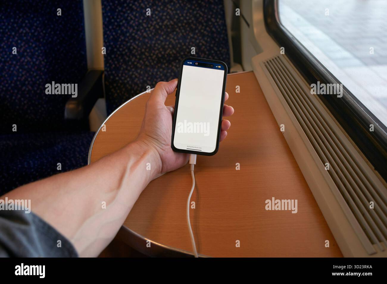 Eine Hand hält ein Smartphone mit einem leeren Bildschirm auf einem Zugtisch neben einem Fenster. Salzkammergut, Salzdomäne, Dachsteingebirge, Österreich Stockfoto