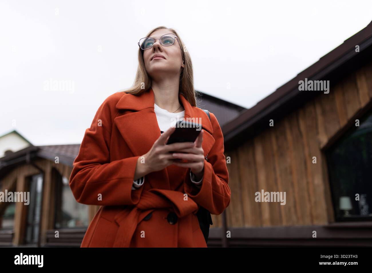 Eine junge Frau mit einem Mobiltelefon in der Hand und einer Sehbrille schaut in die Ferne, das Konzept des Mobilfunkbetreibers Stockfoto