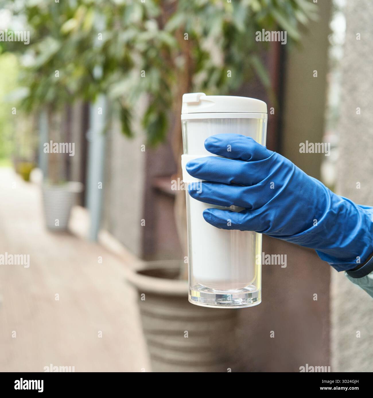 Person mit blauem Handschuh und wiederverwendbarem Reisebecher in urbaner Umgebung Stockfoto