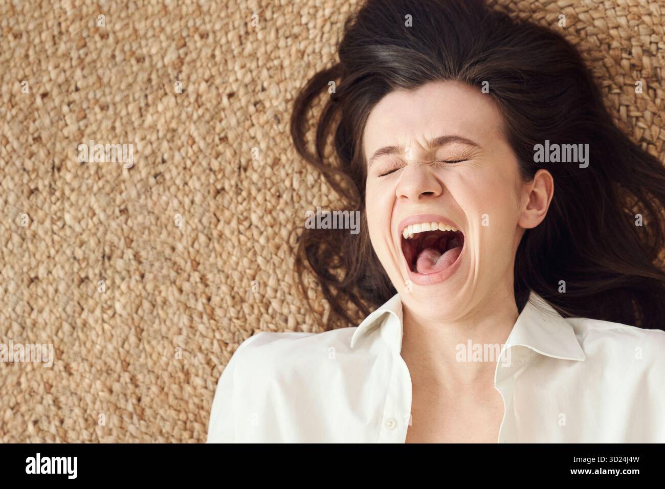 Junge kaukasische Frau lacht mit geschlossenen Augen auf gewebtem textilen Hintergrund Stockfoto