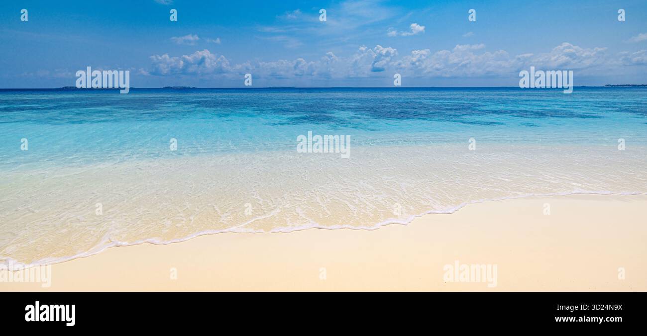 Entspannendes, sonniges Strandpanorama mit ruhigem, blauem Himmel und weichem Sand aus der Nähe. Friedliche Sommeratmosphäre mit Küstenlandschaft. Inspirierende Natur Stockfoto