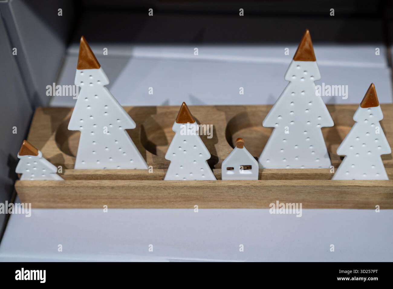Minimalistisch weiße Keramikbäume und kleines Haus auf Holzsockel, festliches Weihnachtsdekor. Stockfoto