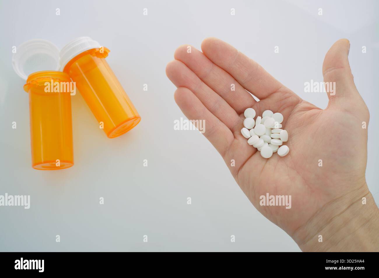 Ansicht von oben nach unten: Hand eines Mannes, der einen Stapel weißer, runder Tabletten hält, mit zwei leuchtend orangen verschreibungspflichtigen Flaschen im Hintergrund. Stockfoto