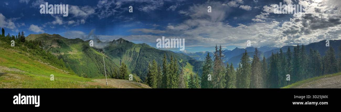 Wunderschönes Bergpanorama mit dichten grünen Wäldern, dramatischen Gipfeln und einem dynamischen bewölkten Himmel. Stockfoto