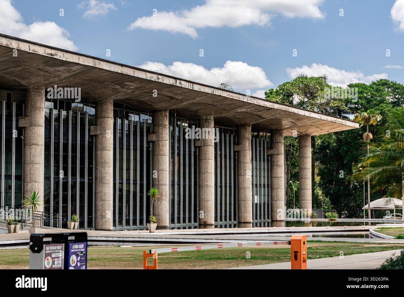 Zeitgenössische Architektur mit einem breiten Betondach, vertikalen Säulen und reflektierenden Fenstern, umgeben von landschaftlichem Grün Stockfoto