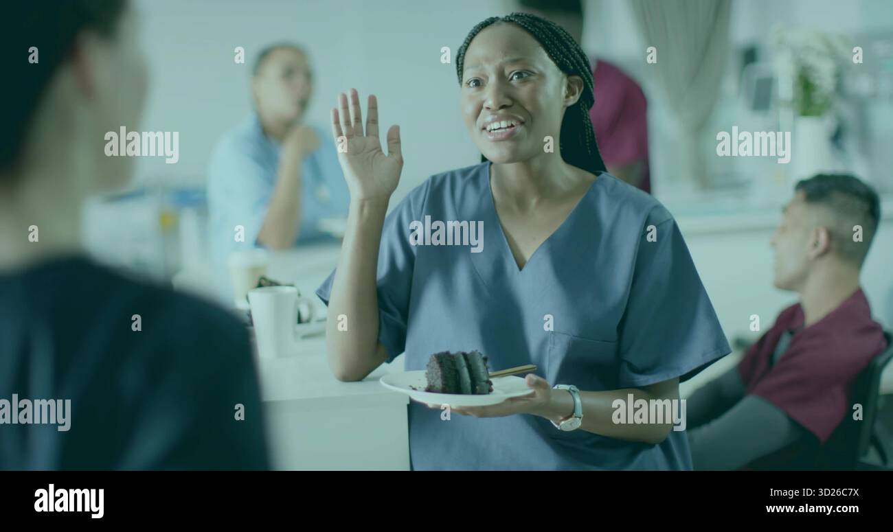 Sprechende Frau in Peelings mit Kuchenscheibe, während sie die Hand in der Lounge des Personals hebt, mit Kaffee-Setup Stockfoto