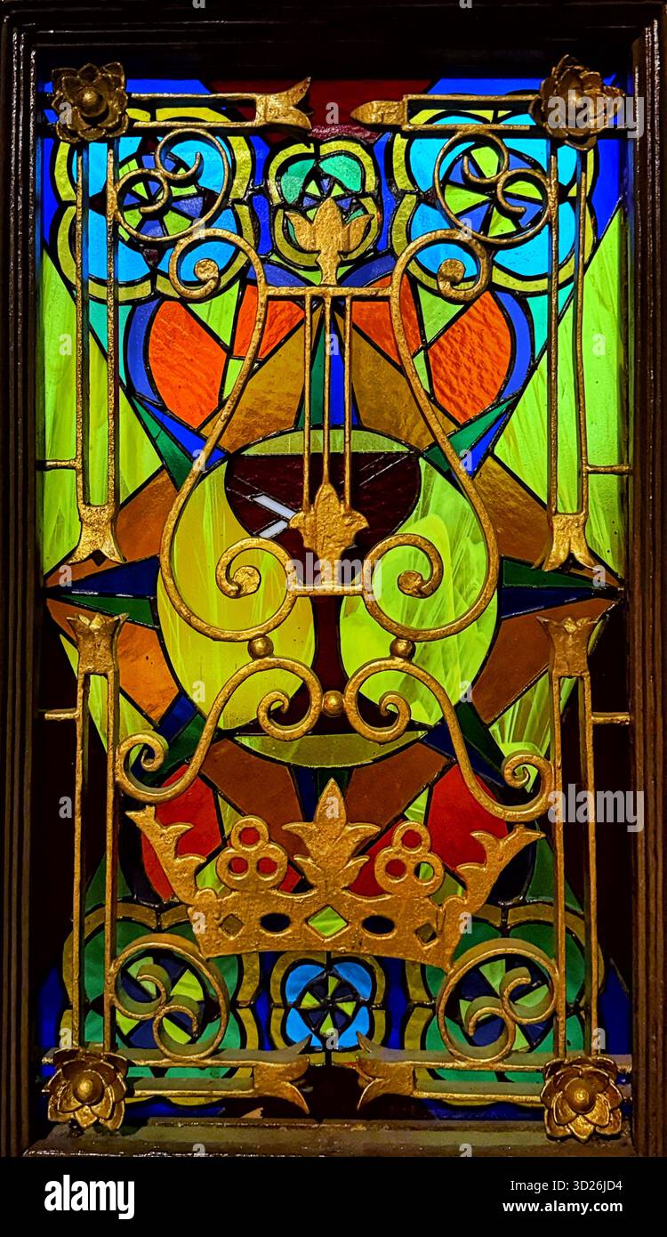 Farbenfrohe Buntglasfenster mit kunstvollen Gold-Schmiedeeisen-Details und symmetrischen geometrischen und floralen Mustern Stockfoto