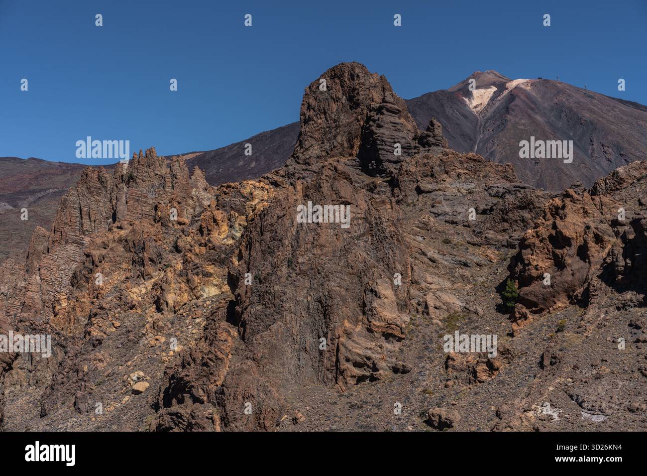 Zerklüftete rötliche vulkanische Felsformationen ragen vor dem Teide unter klarem blauen Himmel in den Vordergrund Stockfoto