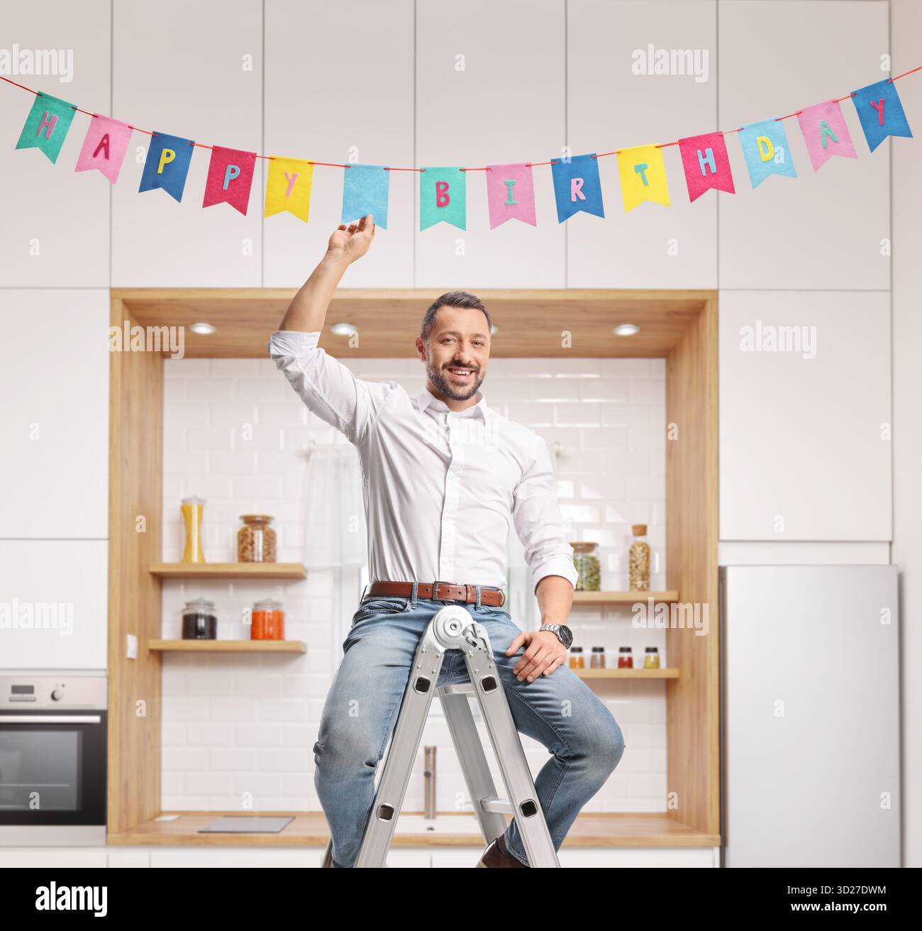 Mann sitzt auf einer Leiter und legt Geburtstagsdekorationsfahnen in eine Küche Stockfoto
