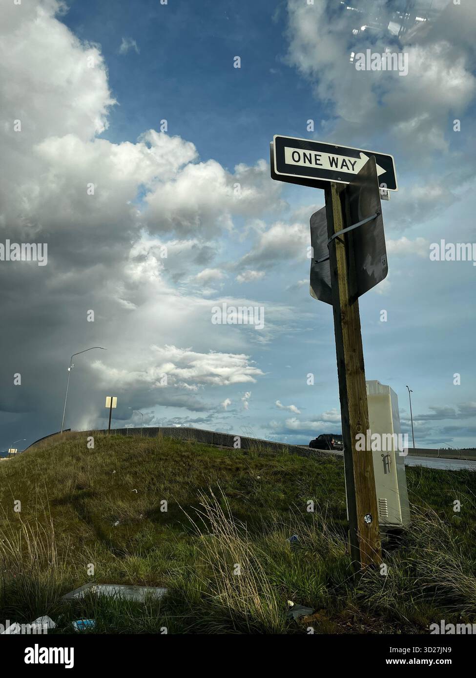 Landstraße mit Verkehrsschild und sanften grasbewachsenen Hügeln unter hellem, bewölktem Himmel - Smartphone-aufgenommenes Stockfoto