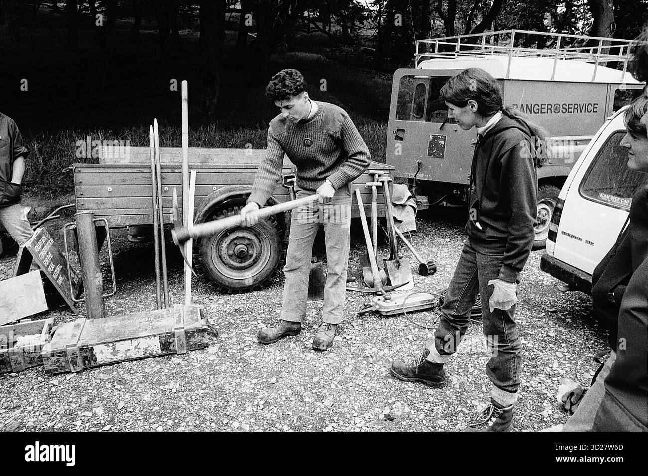 Dieses Schwarzweiß-Foto zeigt einen Park-Ranger, der einer Gruppe von Einzelpersonen während der ersten internationalen Servicereise des Sierra Club in England, Großbritannien, die richtige Verwendung von Handwerkzeugen demonstriert. Der Ranger zeigt aktiv, wie man ein Handwerkzeug verwendet, während andere Teilnehmer beobachten. Das Bild zeigt einen Moment der Schulung und Schulung im Rahmen einer gemeinsamen Naturschutzbemühungen. Stockfoto