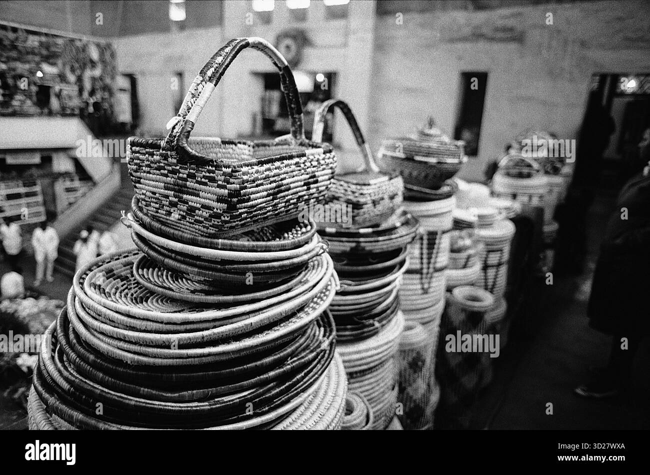 Nairobi’s City Market: Ein Aufruhr der gewebten Tradition. Der City Market, ein geschäftiges Drehkreuz in Nairobi, bietet einen Einblick in Kenias reiches künstlerisches Erbe. Dieses fesselnde Bild zeigt einen beeindruckenden Stapel aufwendig gewebter Körbe, ein Zeugnis für die handwerkliche Handwerkskunst lokaler Handwerker. Die einfarbige Palette betont die Textur und das Detail der Körbe und unterstreicht die anhaltenden Traditionen, die auf diesem pulsierenden Markt weiterhin gedeihen. Stockfoto