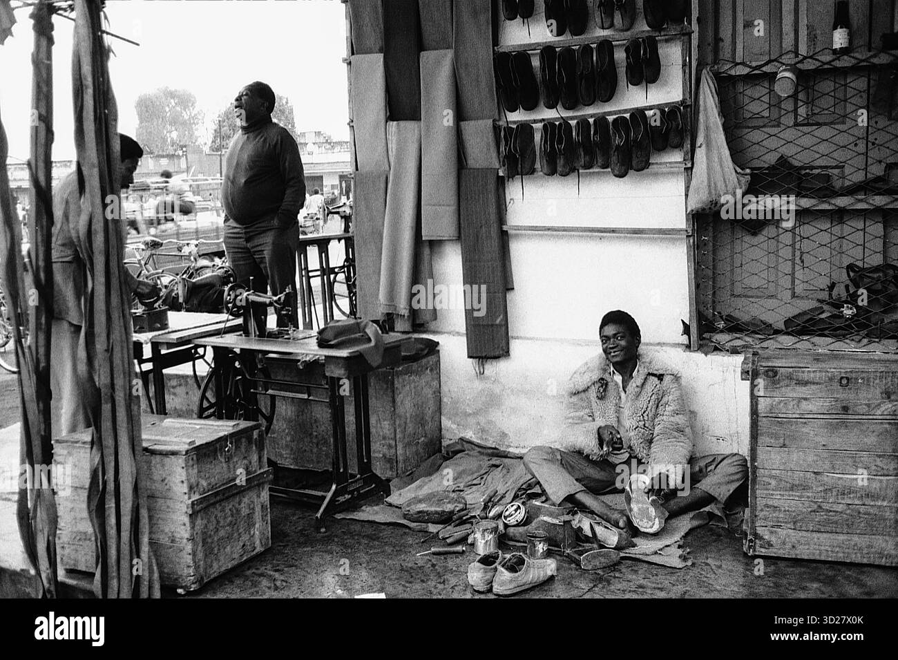 Makuyuni, Tansania – Ein Moment ruhiger Industrie inmitten der belebten Straßen. Dieses Foto zeigt einen Schuhmacher, der fleißig in seinem Geschäft arbeitet, umgeben von Reihen von Schuhen, die auf Reparatur oder Herstellung warten. Die Szene zeigt den täglichen Rhythmus des Lebens in diesem tansanischen Dorf, einem Ort, an dem traditionelles Kunsthandwerk weiterhin gedeiht. Stockfoto