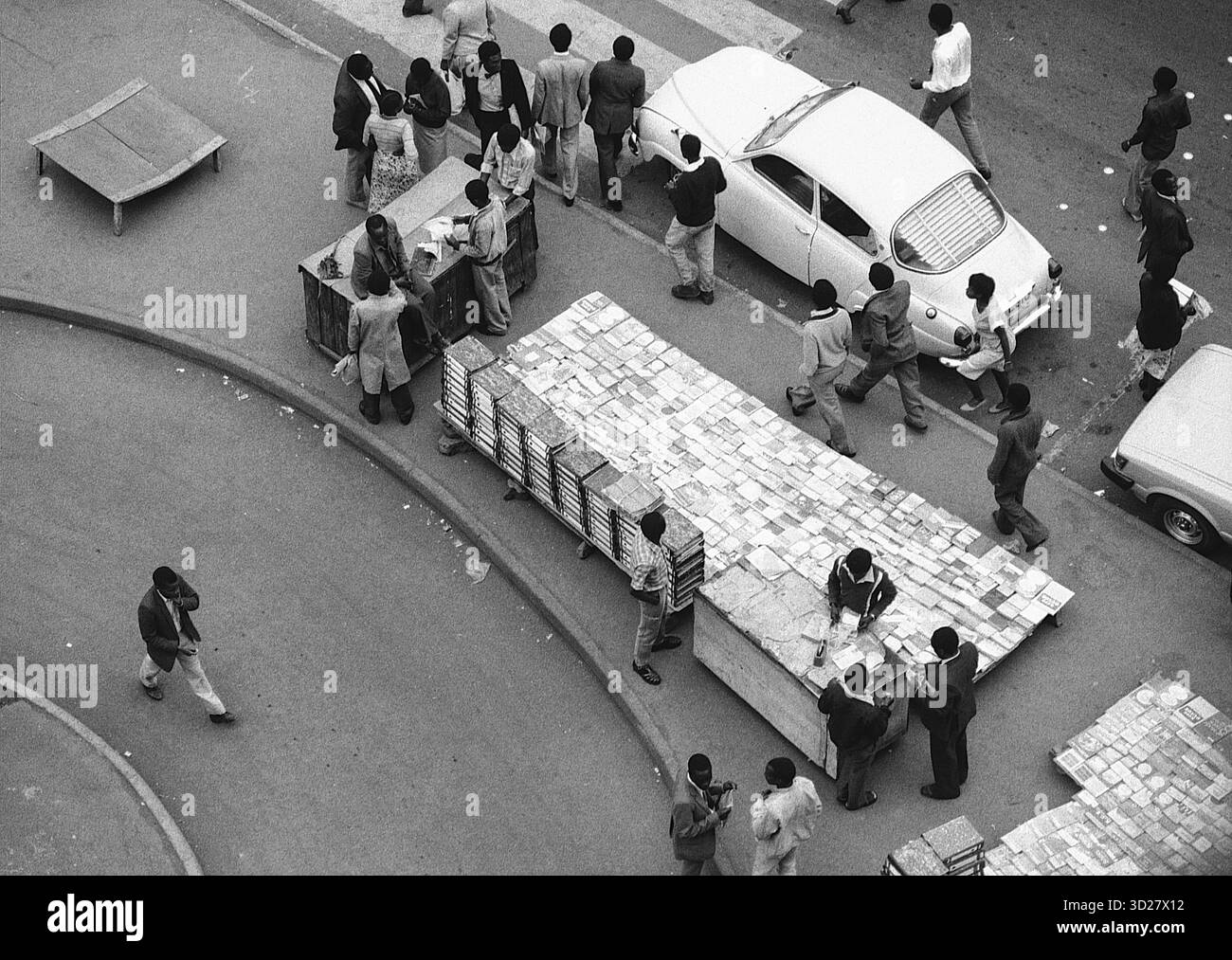 Nairobis pulsierende Straßen pulsieren mit einem einzigartigen Rhythmus. Dieses auffällige Schwarzweiß-Bild fängt einen Moment des Alltags in der kenianischen Hauptstadt ein, wo ein großer Steinstapel sorgfältig durch eine geschäftige Kreuzung gemanövriert wird. Anwohner und Passanten versammeln sich und tragen zur geschäftigen Energie der Stadt bei. Die Szene zeigt den fleißigen Geist Nairobis und die enge Gemeinschaft, die seine urbane Landschaft definiert. Stockfoto