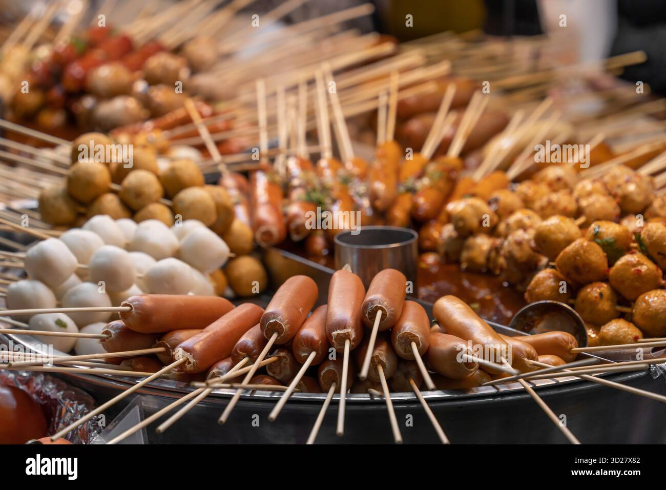 Verschiedene Streetfood-Spieße und frittierte Snacks auf einem runden Grilltablett auf einem Markt. Stockfoto