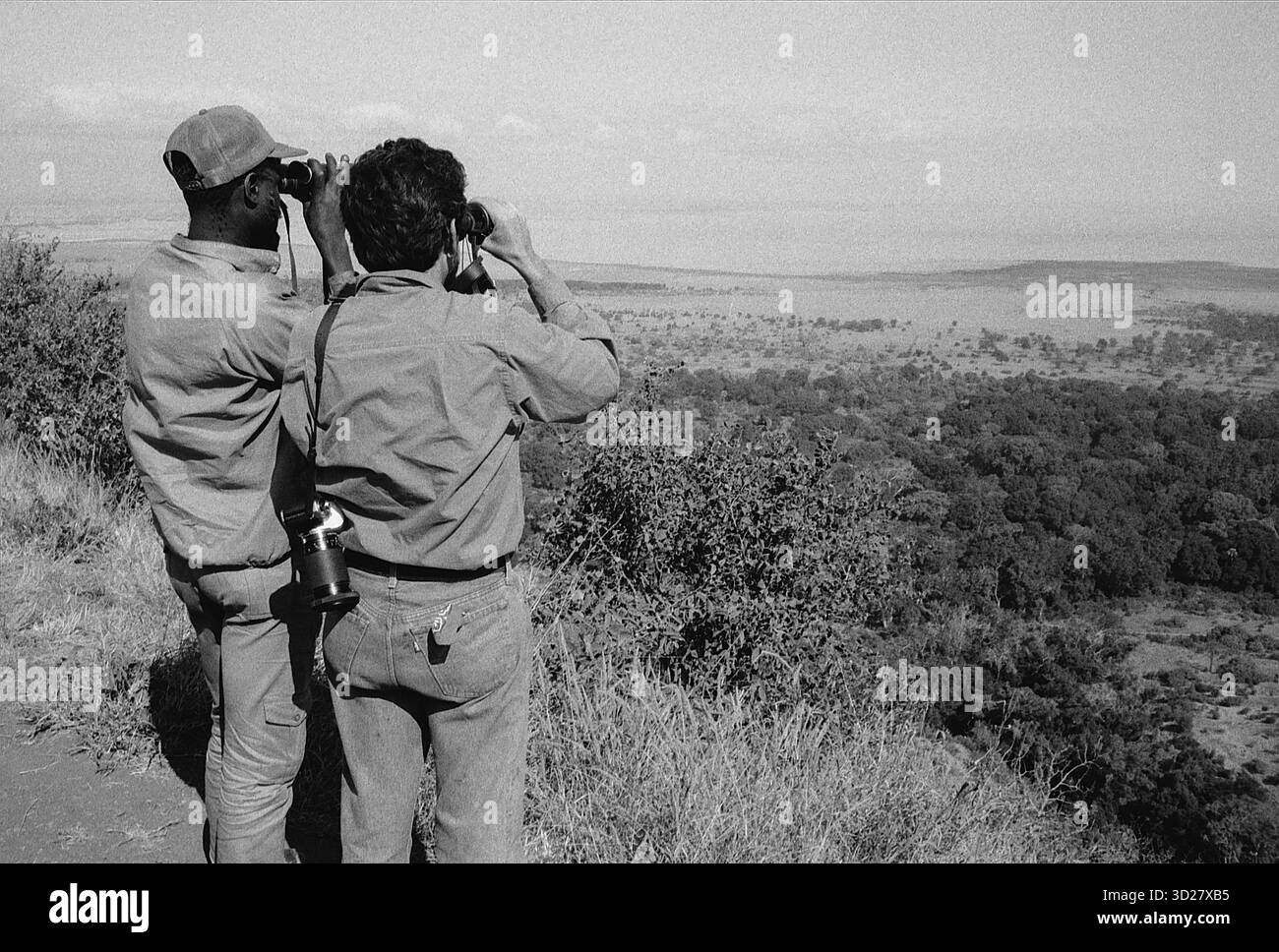 Lake Manyara Aussichtspunkt, Tansania: Zwei Entdecker blicken durch ein Fernglas und vermessen die Weite der tansanischen Savanne. Der ferne Horizont deutet auf die unglaubliche Tierwelt hin, die im Manyara-Nationalpark gedeiht, einem Paradies für Elefanten, Giraffen und unzählige andere Arten. Stockfoto