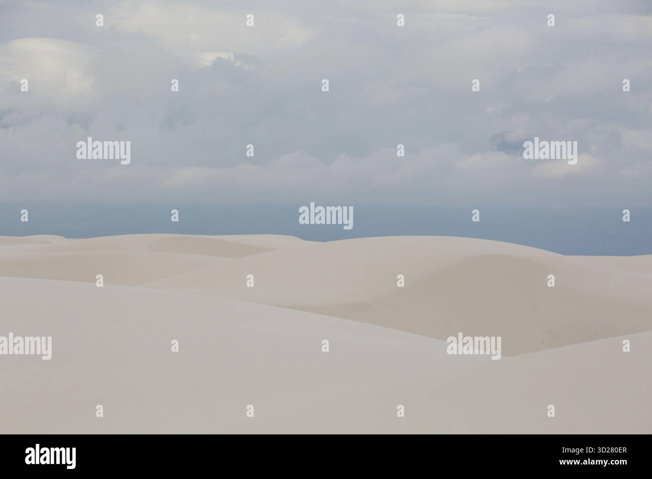 Weiche, glatte Sanddünen erstrecken sich über die Landschaft, während dunkle Wolken über sich ziehen. Die Szene fängt die Ruhe der Natur bei Sonnenaufgang in White Sands ein Stockfoto