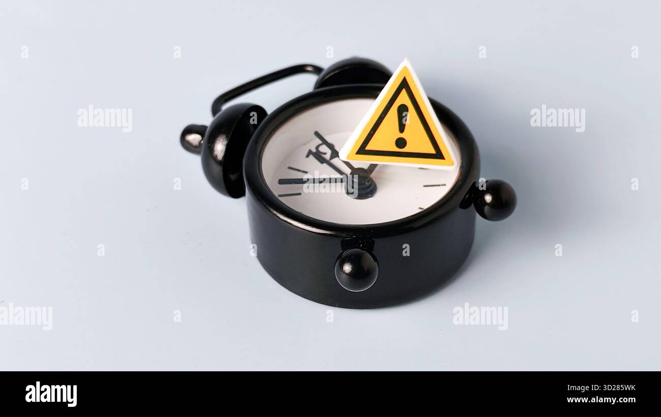 Kritisches Deadline- und Zeitmanagement-Risiko: Warnschild auf schwarzem Wecker Stockfoto
