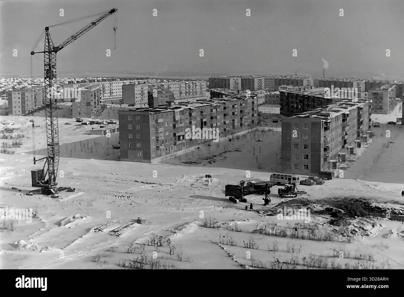 Archiv Schwarzweißfoto aus den 1970er Jahren in Sloviansk, Ukrainische SSR. Dies ist ein Hochwinkelblick auf den massiven Bau des Mikroviertels Artema, insbesondere des Unterbezirks „Molodezhnaya“. Ein hoher Turmkran dominiert den Vorderboden auf dem schneebedeckten Boden, mit Lkws in der Nähe. Im Hintergrund werden neue 5-stöckige Paneelgebäude („Pyatietazhki“) gezeigt, die das neue Wohngebiet bilden. Die gesamte Landschaft ist mit tiefem Schnee bedeckt. Dieses Bild dokumentiert die großräumige sowjetische Stadtentwicklung. Stockfoto