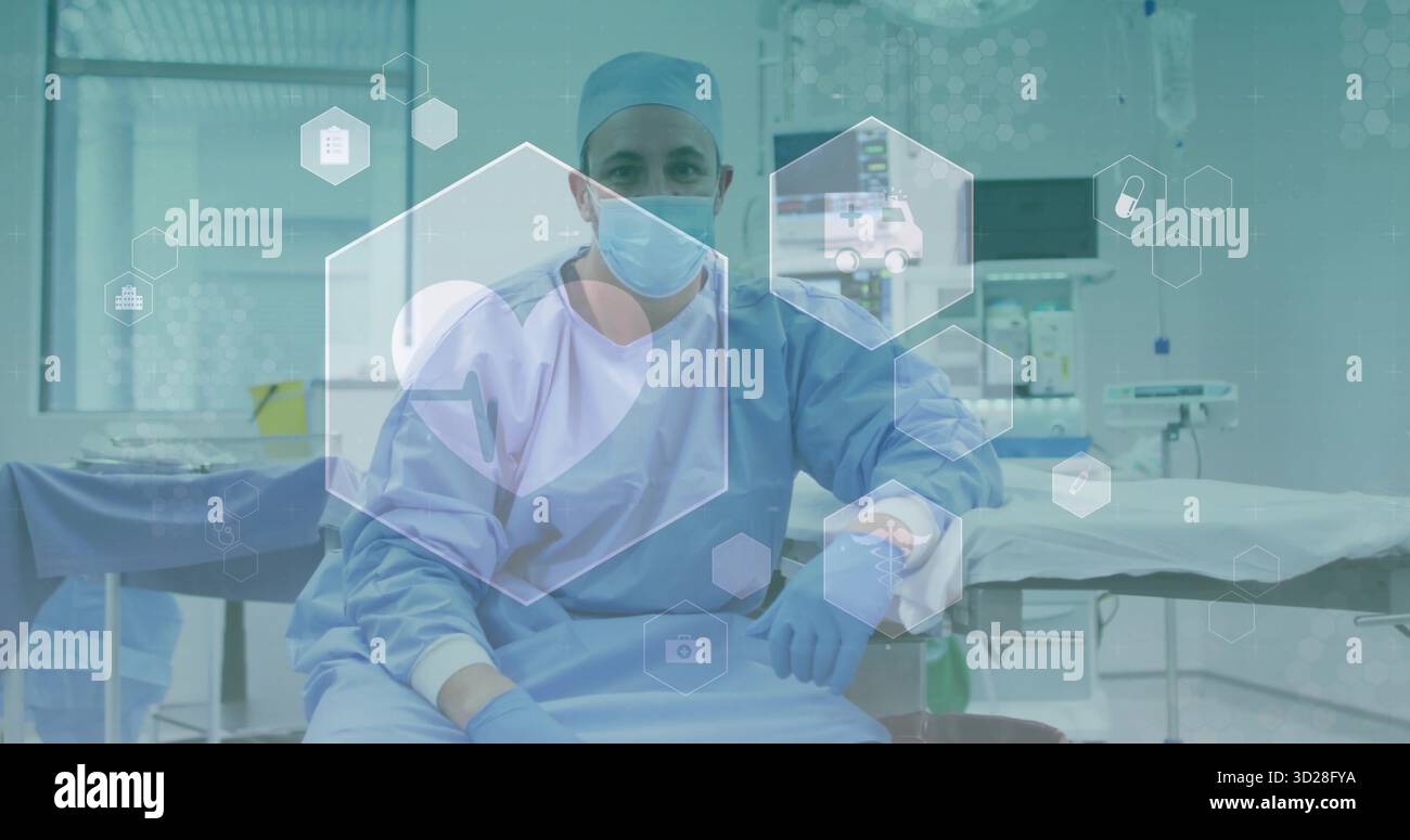 Sitzender männlicher Chirurg mit blauen Peelings mit Maske und Handschuhen im Operationssaal mit Monitoren Stockfoto
