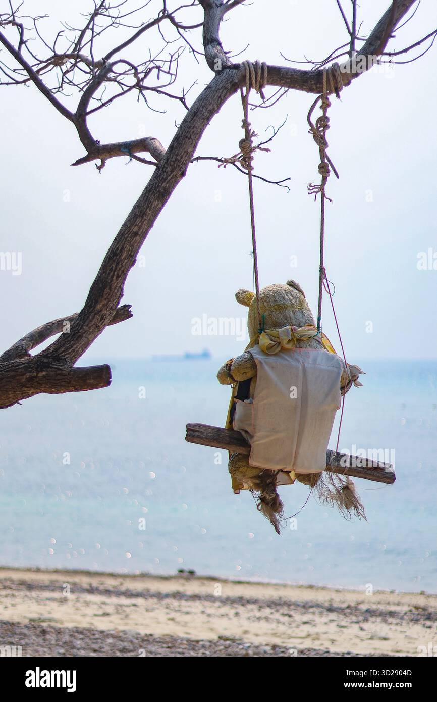 Ein alter Teddybär sitzt auf einer Schaukel am Strand auf einer ruhigen Insel. Ich sah es und fühlte mich einsam und allein. Ich fühle mich, als würde ich jemanden vermissen. Alte Teddybären wurden geworfen Stockfoto