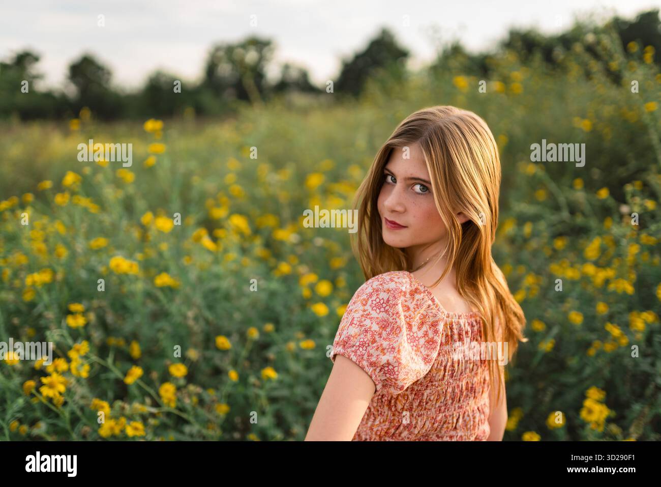 Das Mädchen mit Blumenoberteil blickt zurück, während es im Wildblumenfeld steht Stockfoto