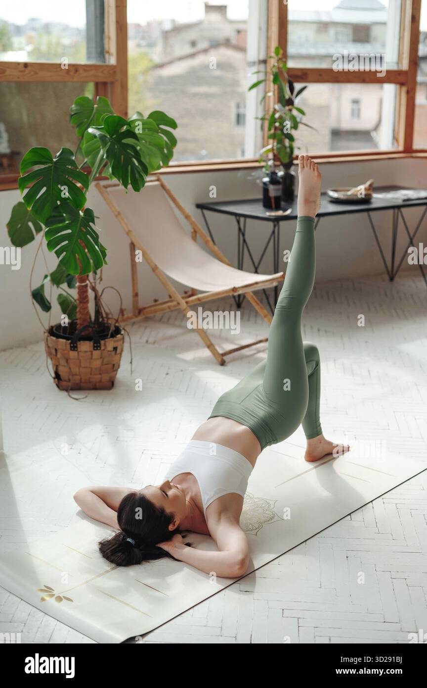 Frau übt Yoga in Innenräumen mit Beinlift-Pose Stockfoto