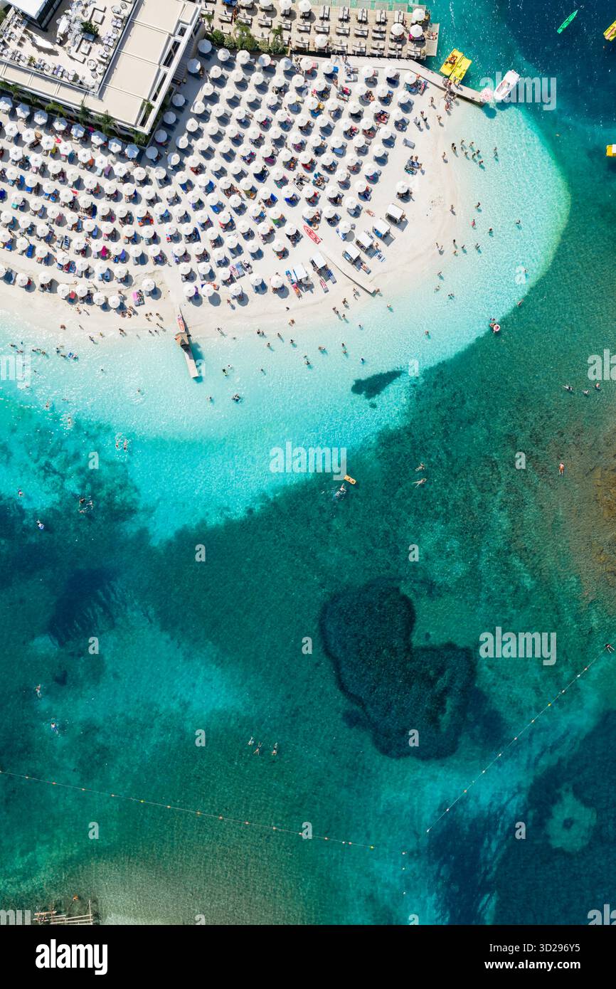 Aus der Vogelperspektive auf einen pulsierenden Strand mit dicht gepackten Sonnenschirmen, die Schatten auf den weißen Sand werfen, im Kontrast zum azurblauen Meer, Ksamil, Vlor, Albanien. Stockfoto